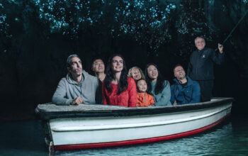 A group of people sitting in a boat inside a dark cave illuminated by glowing blue lights, likely from glowworms on the cave ceiling.