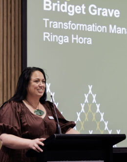 A side angle of a wahine Māori (Māori Women) standing behind a podium and giving a presentation.