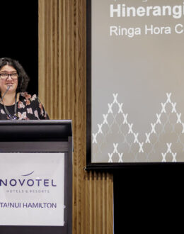 A wahine Māori (Māori women) standing behind a podium and giving a presentation.