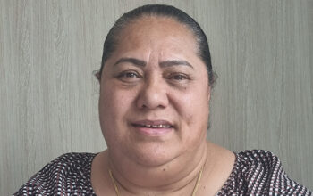 Close up of a person wearing a checkered top and gold necklace.