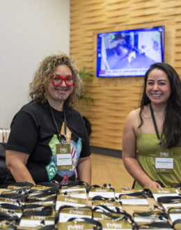 Two wahine Māori (Māori women) sitting down in front of a desk full of lanyards.