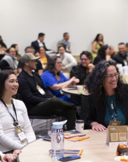 A conference room full of people smiling and sitting down at circular tables.