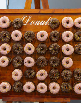 A wooden sign with chocolate and strawberry donuts hanging from it.