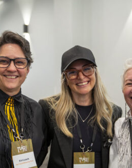 A close up of three people posing together for the camera. In the background is a big hall.