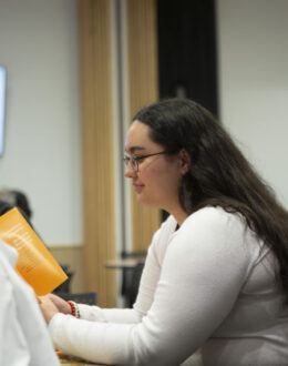 A side angle of a person sitting down and reading a pamphlet.