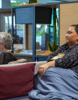 A side angle of two people sitting on a grey sofa.