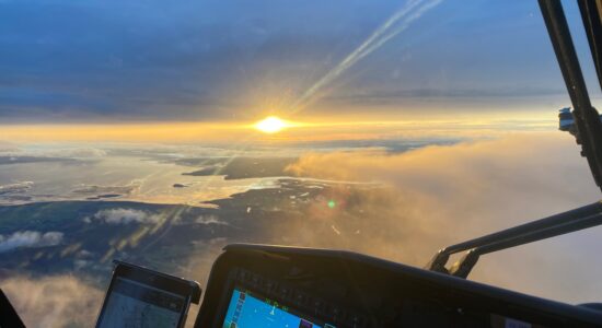 A inside of a helicopter with a sunset in the background.