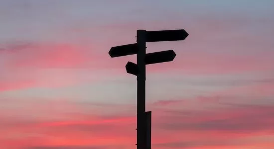 A close up of a street sign, with a pink sunset hue in the background.