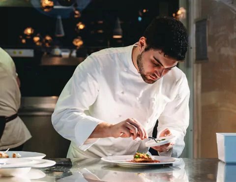 A close up of two people in a commercial kitchen preparing food.