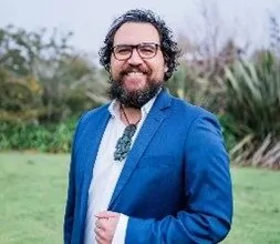 A person smiling and wearing a blue jacket, with a white shirt.