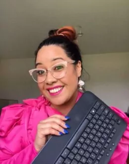 A close up of a person smiling while holding a keyboard in their hands. They are wearing a bright pink dress.