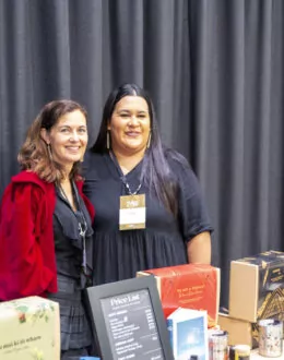 Two people standing behind a table. The table in front of them has a range of candles for sale.