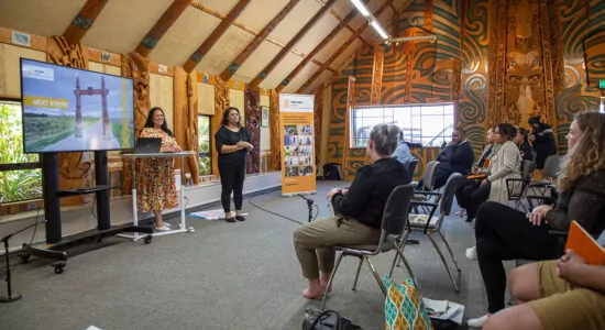 Two women presenting to a group of people within a marae